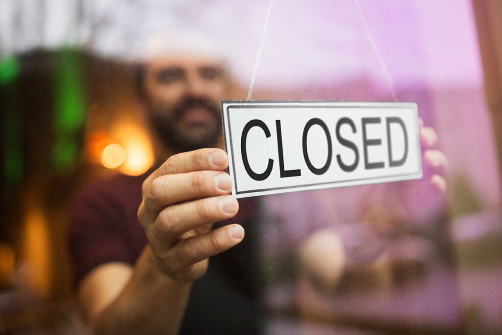 Ein mann steht vor einer Scheibe und dreht ein Schild um, auf dem "Closed" steht