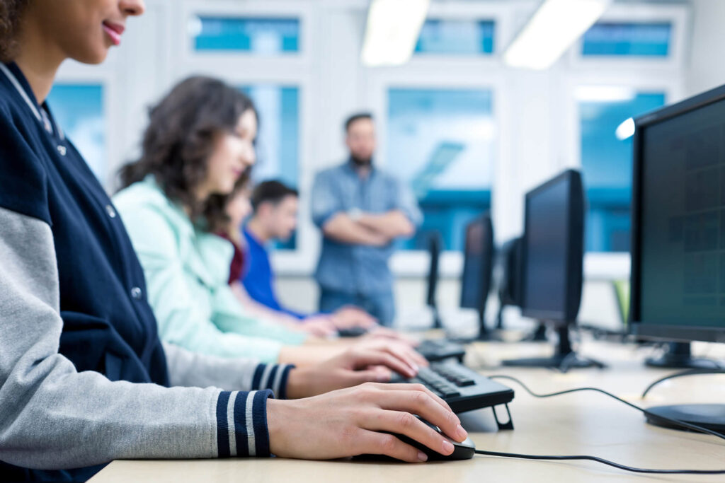 Mehrere Personen sitzen nebeneinander an Desktop PCs