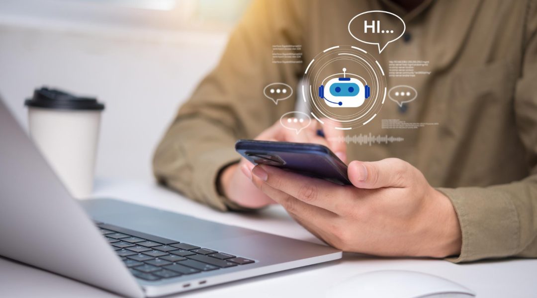 Eine Person sitzt vor einem Laptop an einem Tisch. Sie hält ein Smartphone in der Hand. Über dem Smartphone sind Grafiken die auf einen AI Bot hinweisen.
