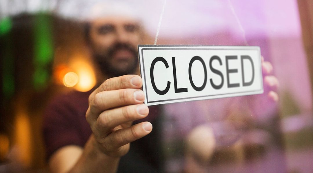 Ein mann steht vor einer Scheibe und dreht ein Schild um, auf dem "Closed" steht