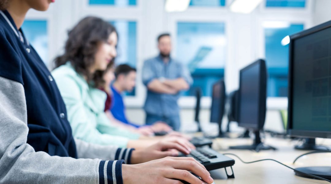 Mehrere Personen sitzen nebeneinander an Desktop PCs
